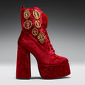 Red velvet platform boot with gold embellishments on a gray background