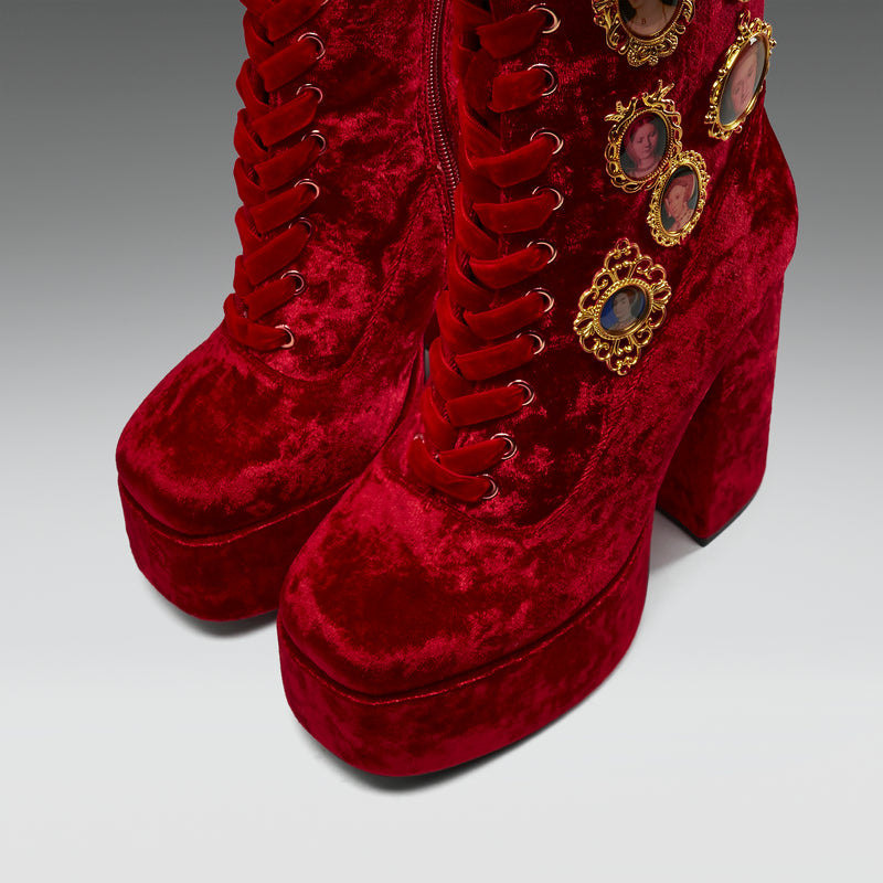 Red velvet platform boots with gold embellishments on a gray background