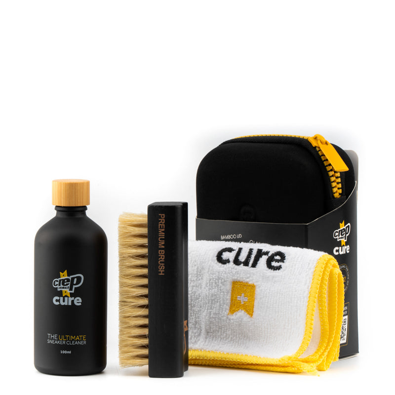 Sneaker cleaning kit with dark cleaner bottle, brush, and yellow-edged microfiber cloth