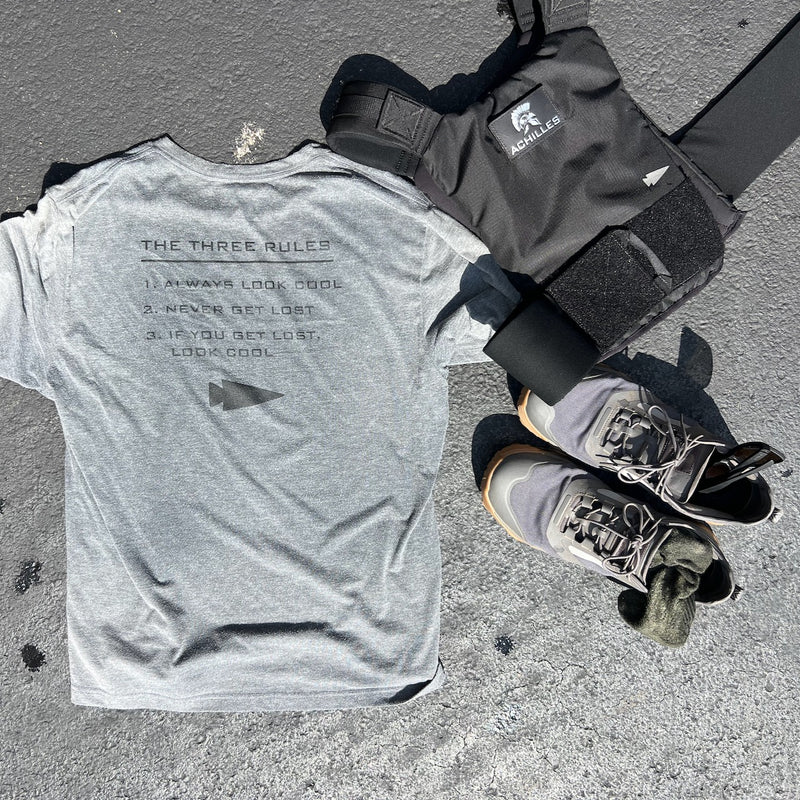 A gray Three Rules Tee - Unisex Tri-BlendX, black weighted vest, and gray sneakers are laid out on a sunny outdoor surface—gear that keeps you looking cool wherever your workout takes you.