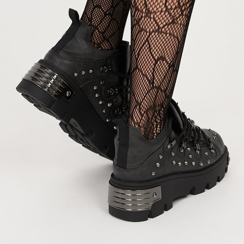 Black studded boots worn with fishnet stockings on a light gray background