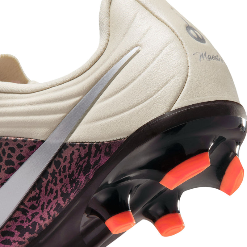 Close-up of youth soccer cleats: cream upper with silver stripe and black outsole with orange studs