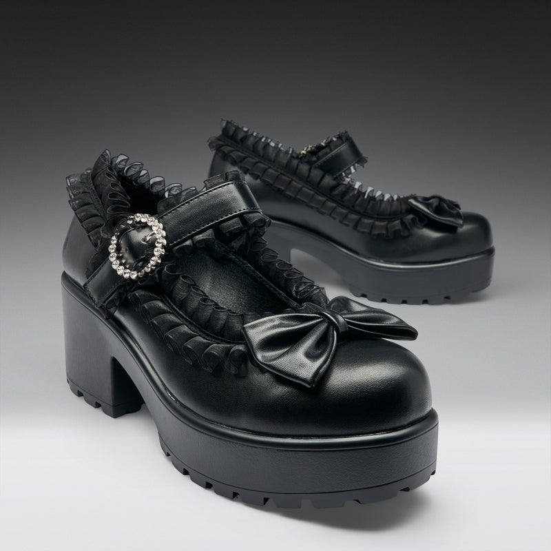 Black platform shoes with ruffles and a bow on a gradient background