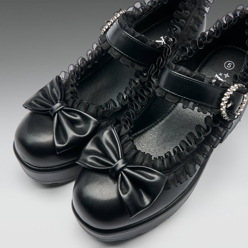 Black platform shoes with bows and decorative straps on a gray background
