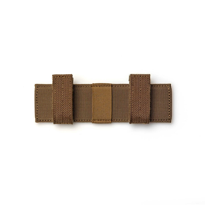 The Tourniquet Attachment is a brown nylon strap with two loops and reinforced stitching, designed as a compact book-style organizer, shown laid flat on a white background.
