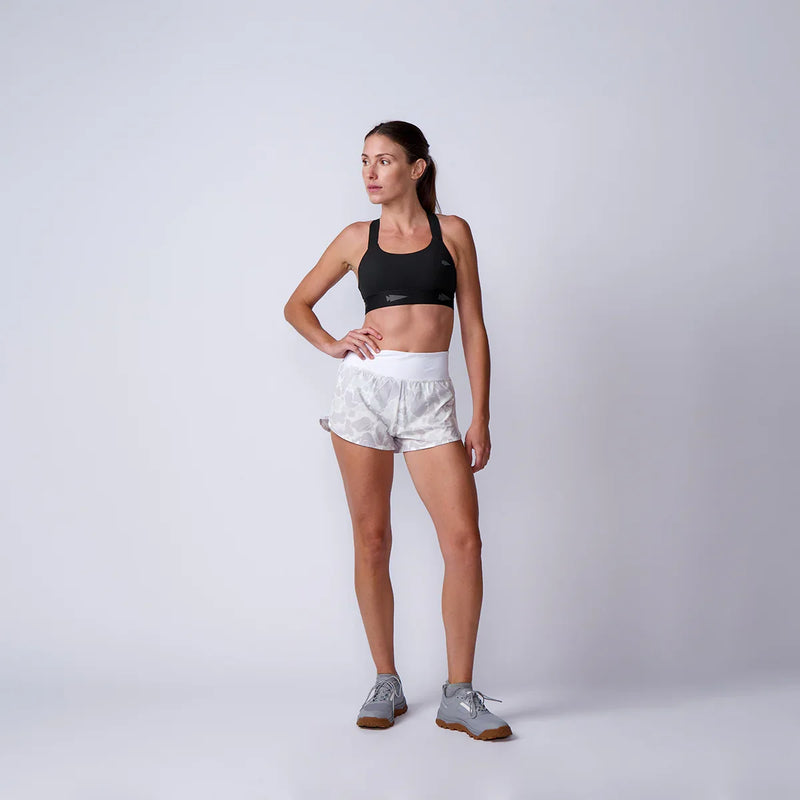 Woman wearing GORUCK athletic gear, black sports bra, camo shorts, grey rucking shoes in studio