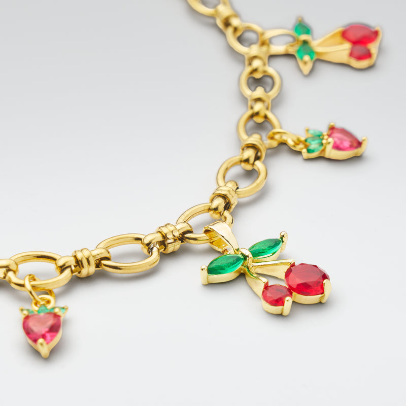 Gold bracelet with cherry-themed charms on a light gray background