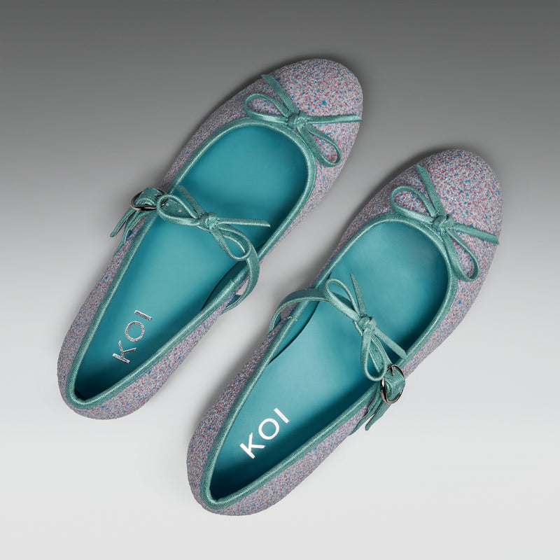 Pair of light blue flats with glittery gray accents and bow details on a gray background.