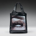 Black tote bag with eye design and 'Koi' branding on a gray background