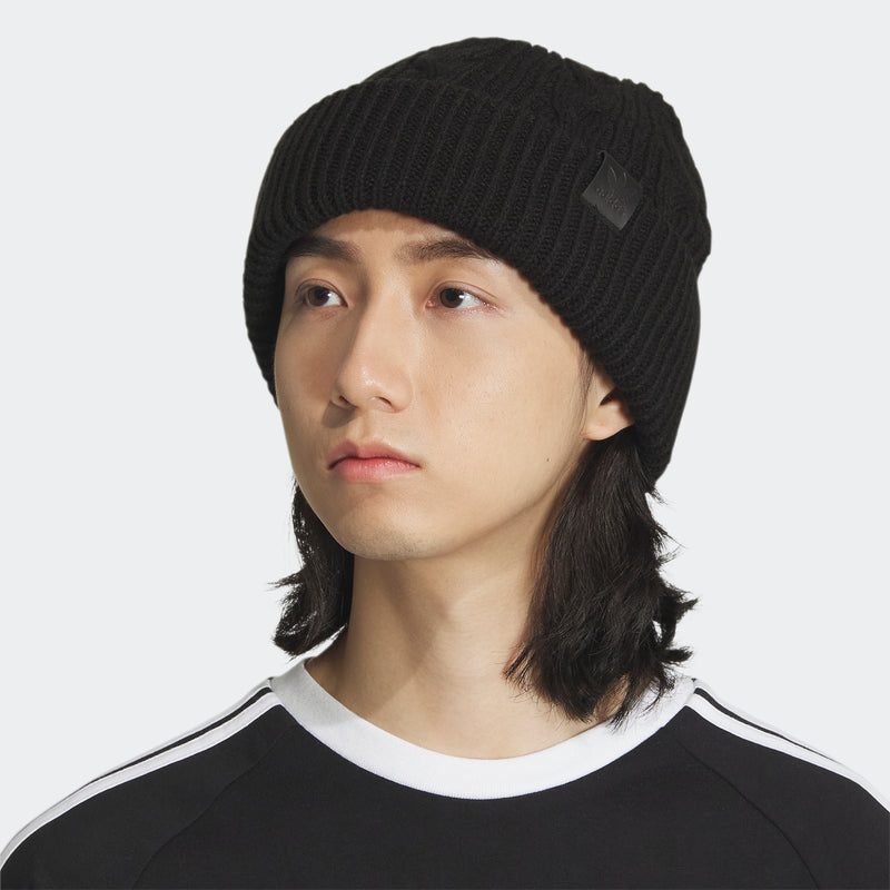 Black cable-knit beanie on model, ribbed knit with small side logo patch.
