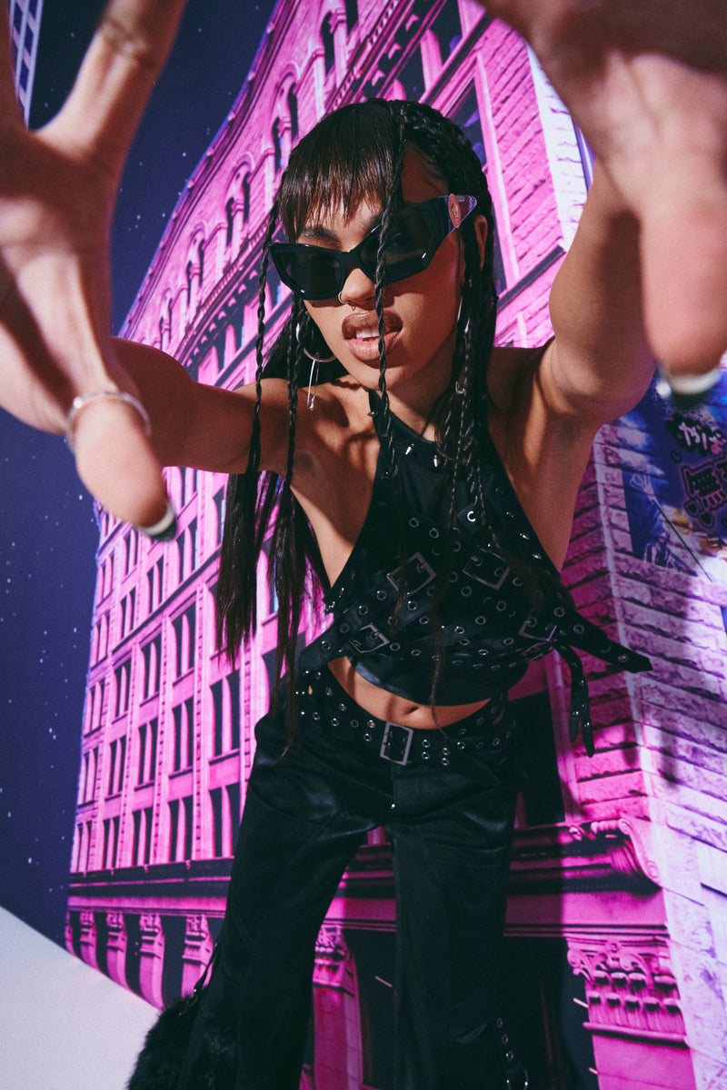 Person in black outfit with sunglasses against a pink building background