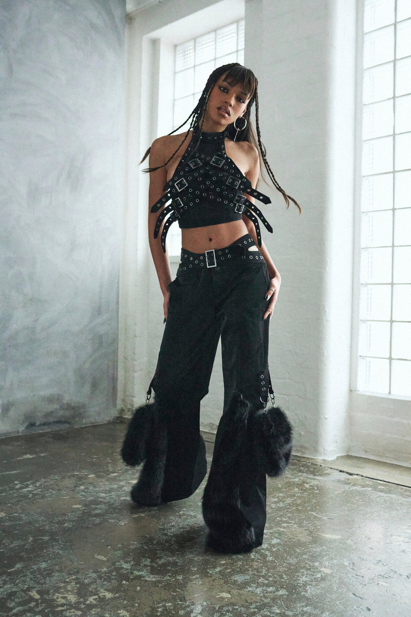 Person wearing a black outfit with flared pants and a crop top in a minimalistic setting.