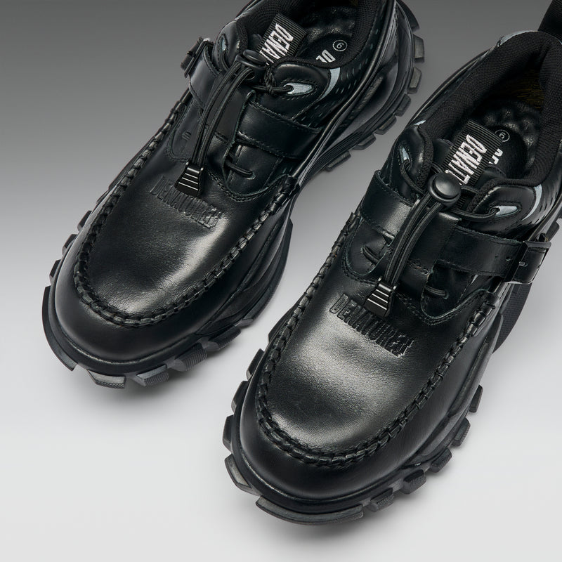 Pair of black leather shoes with unique sole design on a light gray background