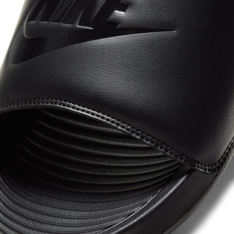 Men's black slide sandals close-up: stitched strap edge and textured footbed