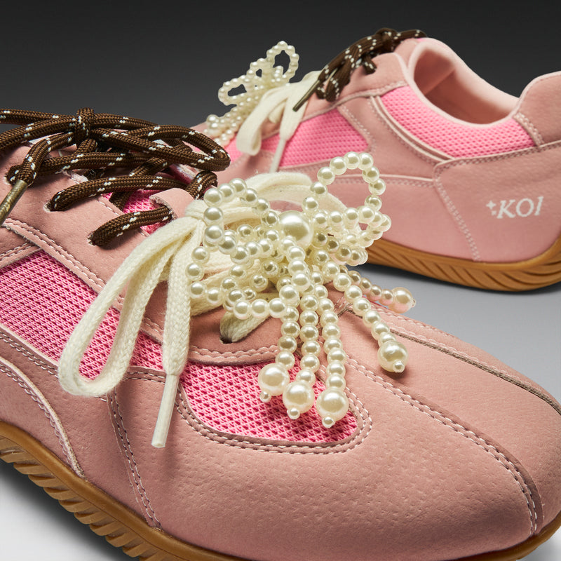 Pink sneakers with decorative laces and pearls on a gray background