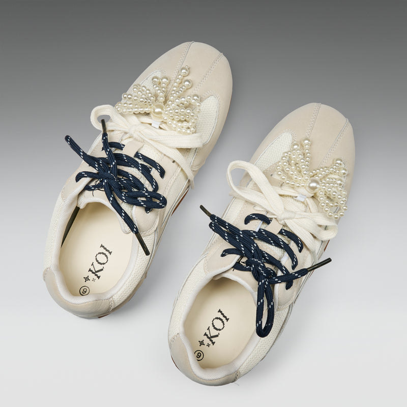 Pair of white sneakers with decorative elements on a gray background