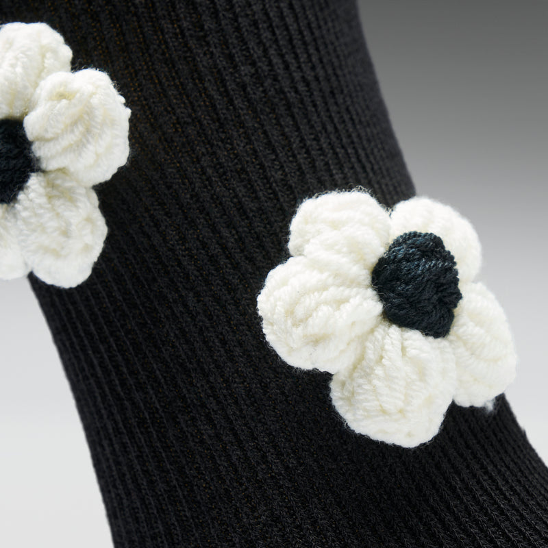 Black sock with white knitted flowers on a gray background