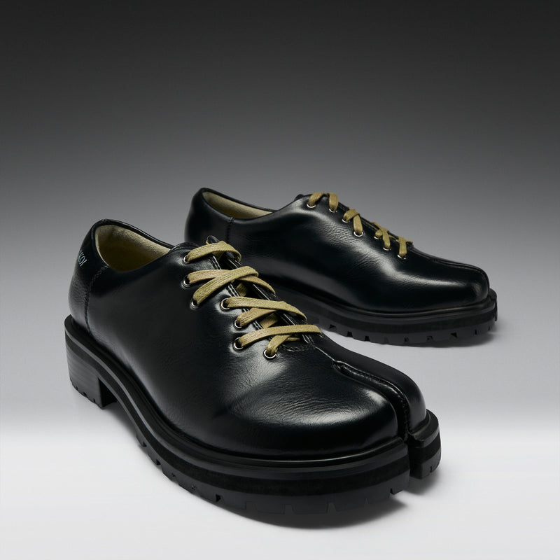 Pair of black leather shoes with green laces on a gradient background