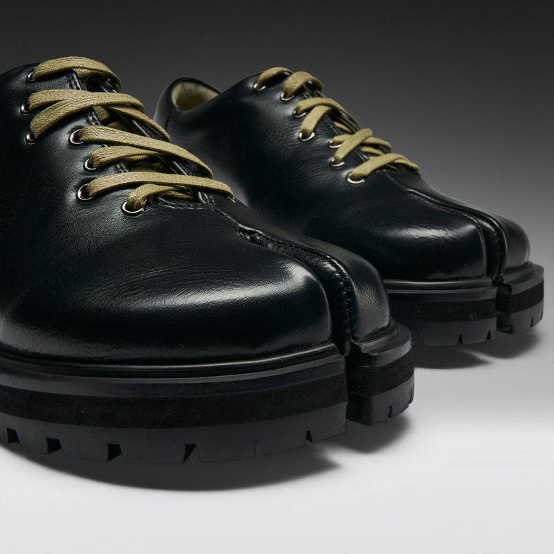 Pair of black leather shoes with green laces on a gradient background