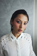 Woman wearing a white blouse with black details against a gray background