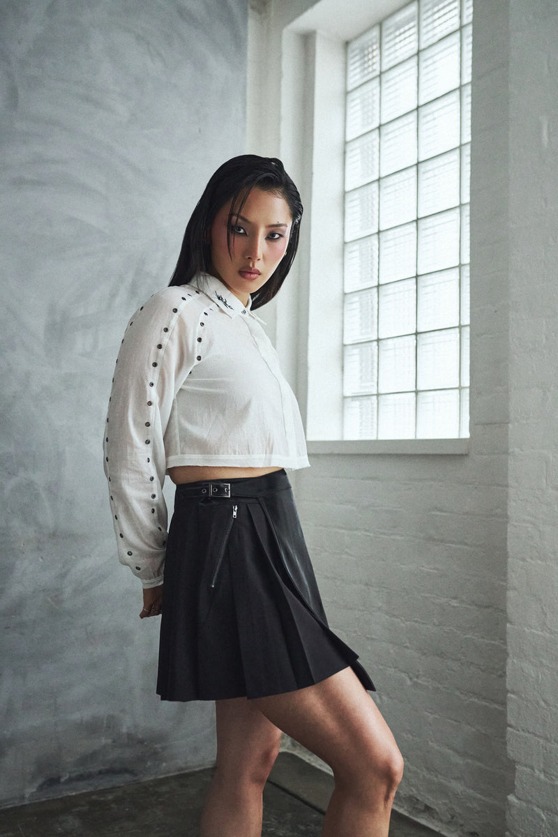 Woman wearing a white blouse with black accents and a black skirt in a room with large windows.