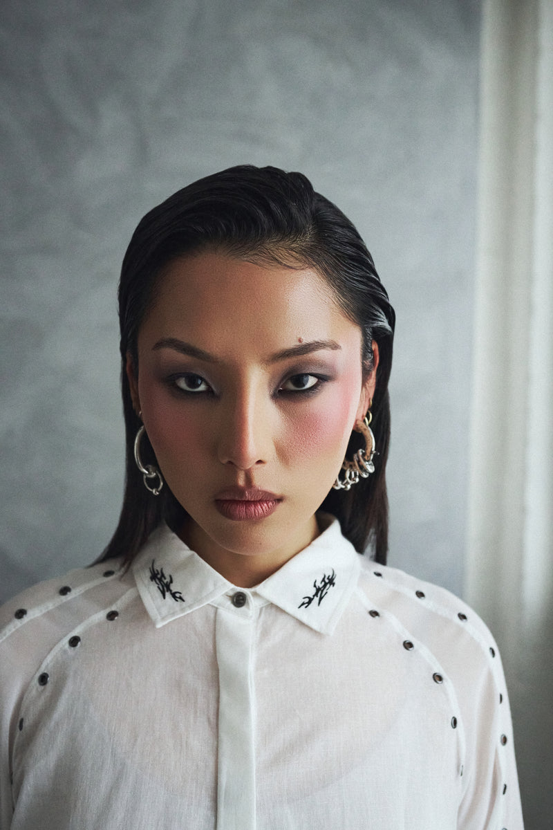 Woman wearing a white blouse with black patterns against a gray background