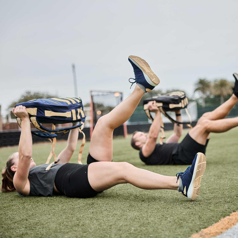Two people rucking with GORUCK sandbags while exercising on a turf field outdoors