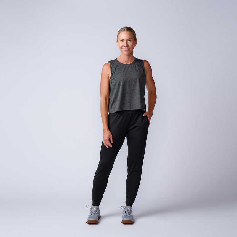 Woman in a gray sleeveless top, Women’s Training Performance Joggers, and sneakers stands and smiles against a plain background.