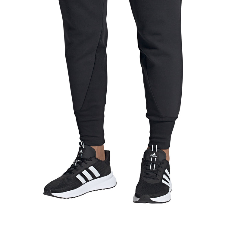 Men's black adidas sneakers worn by model, white stripes and white cushioned sole