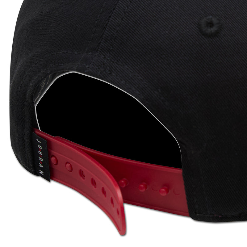 Black snapback cap with red buttoned strap and stitched panels