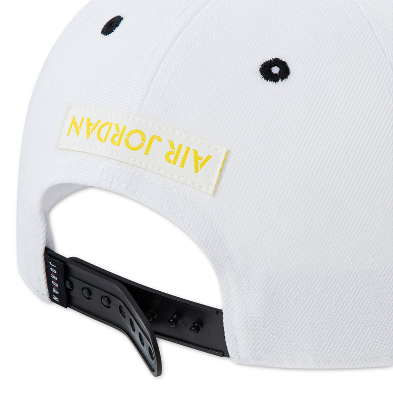 White snapback cap close-up with black strap and yellow logo label